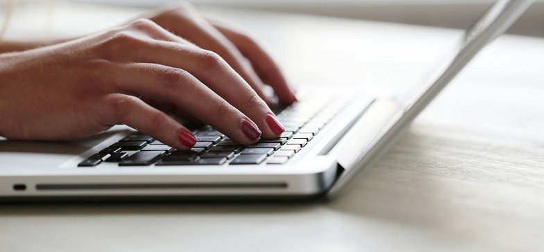 Zbliżenie na kobiece dłonie - osoba fotografowana pracuje na komputerze.